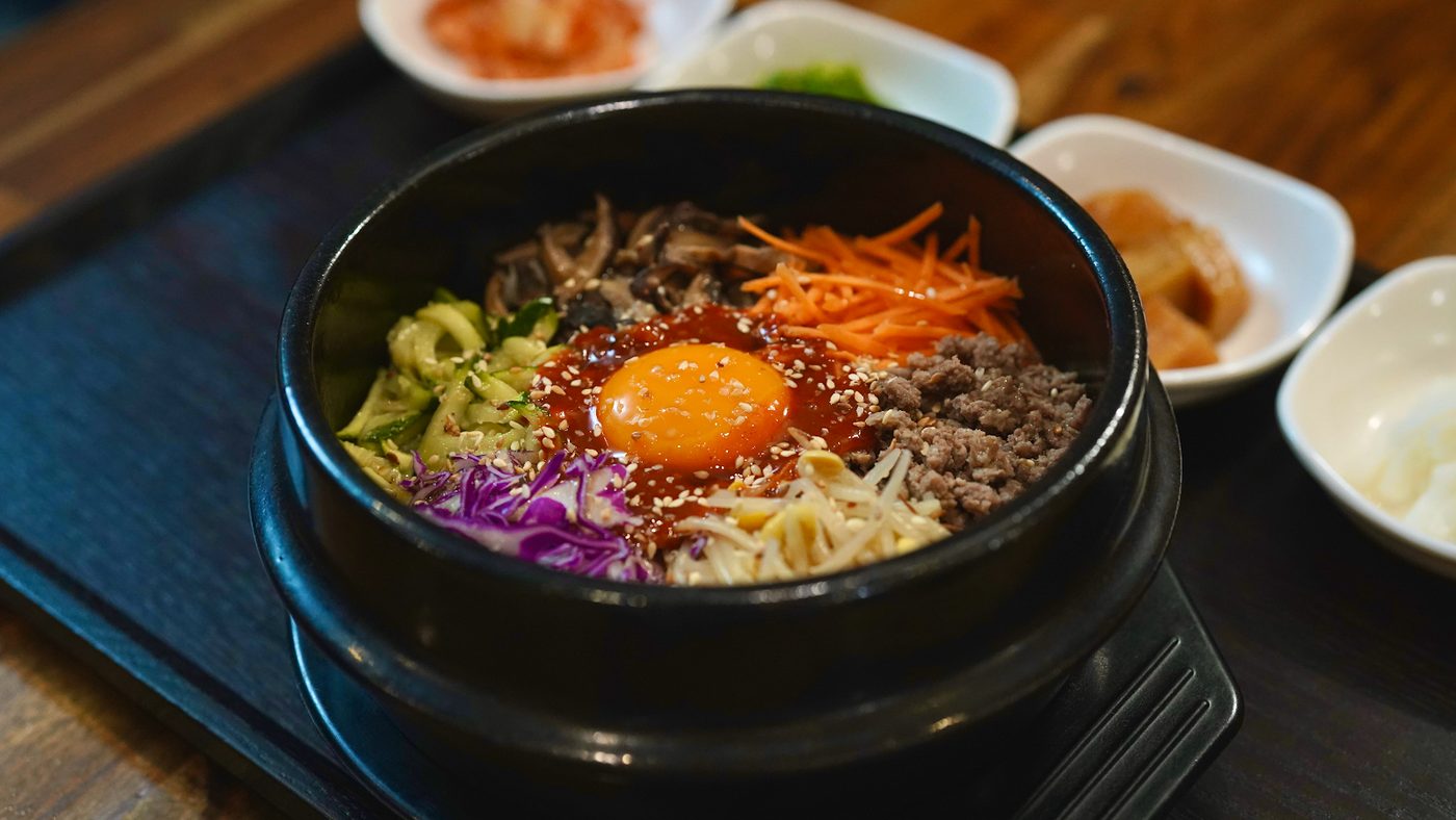 Bibimbap in a black stone bowl, vegetables and minced meat laid around a raw yolk