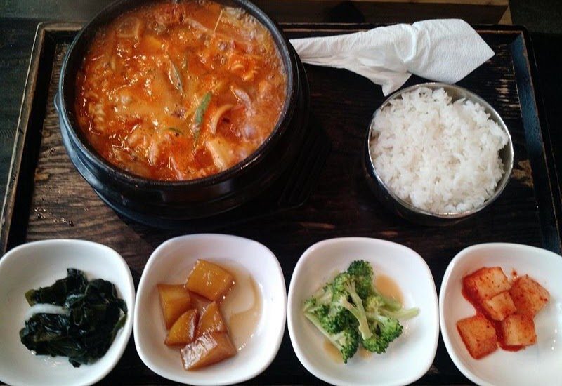 A black stone pot of red stew, filled right up to the rim, with rice beside it