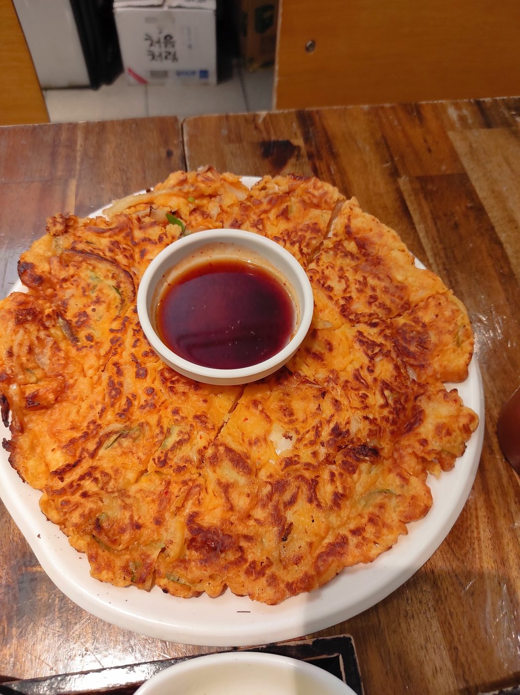 A savoury pancake the width of the plate, cut into wedges around a bowl of dark dipping sauce